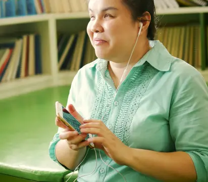 Mulher com camisa verde segurando um smartphone que lê a tela do Portal de Acessibilidade da MRV